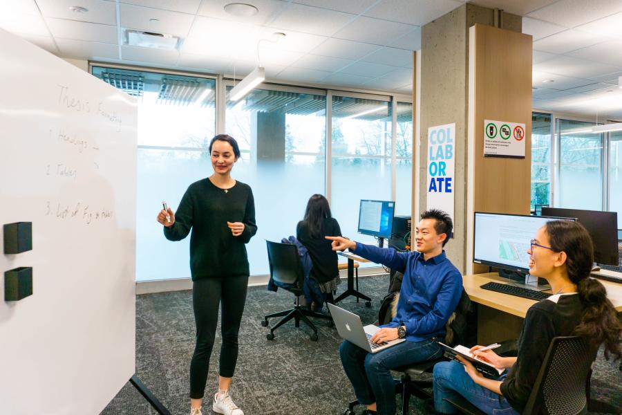 Students presenting in the research commons in front of a whiteboard, one of them is pointing