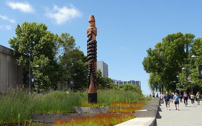 Looking up past the cascading water feature on University Blvd. to the Musqueam Post. 