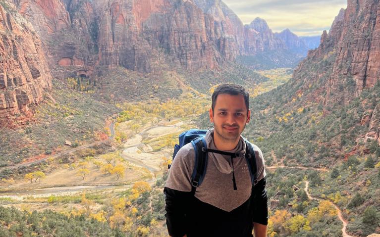 person standing outdoors in front of a scenic landscape with a canyon in the background