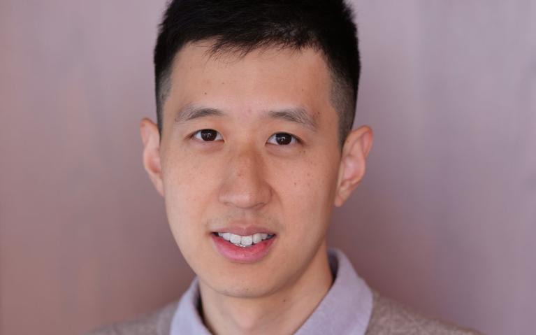person with grey sweater and light background smiling