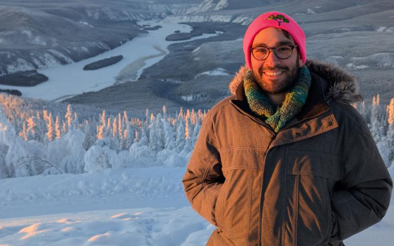 person in a thick winter coat standing in the snow with tundra behind them