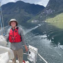 Tyler De Jong wearing a lifejacket on a boat with mountains in the background