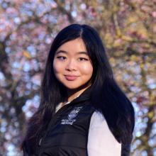 Woman wearing black jacket standing in front of blurry tree background