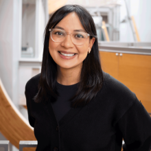 Woman with black shirt and black hair smiling with glasses